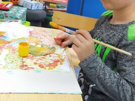 chłopiec siedzi przy stole i wykonuje pracę plastyczną, maluje pędzlem