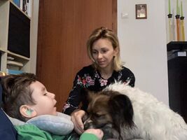 Pies dotyka nosem dłoni ucznia, dogoterapeutka siedzi obok