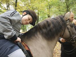 Sebastian przełamuje lek przed koniem, siedzi na koniu i pochyla głowę w kierunku szyi konia, z przodu mężczyzna trzyma konia za wodze