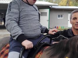 chłopiec siedzi na grzbiecie konia o imieniu Hejnał, obok asekuruje hipoterapeuta