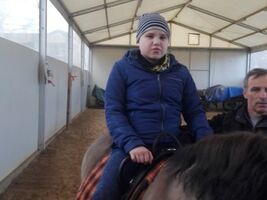 chłopiec siedzi na grzbiecie konia o imieniu Hejnał, obok asekuruje hipoterapeuta